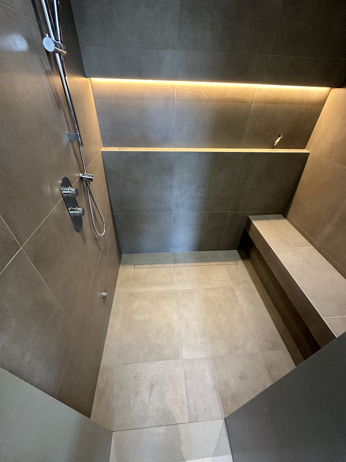 Walk-in shower with large-format porcelain walls, a lit full-width niche and a tiled built-in bench