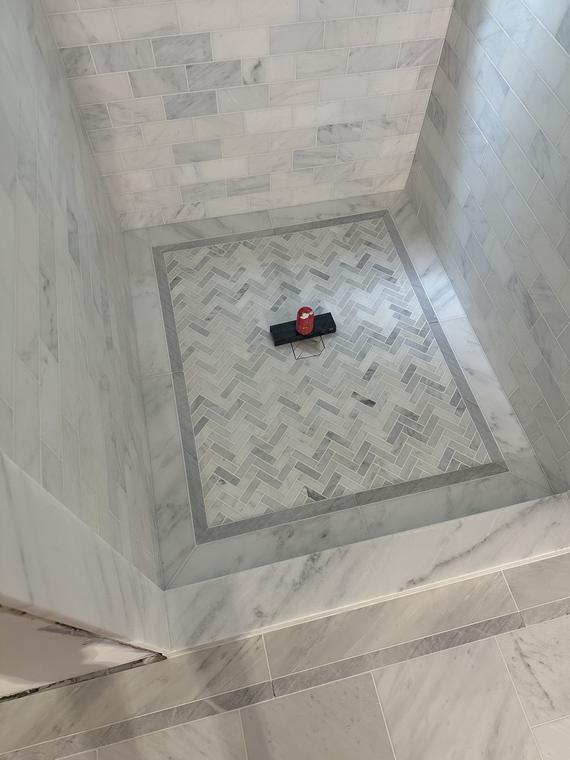 Herringbone marble mosaic shower floor framed by a border